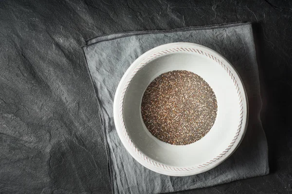 Sementes de chia na placa branca na vista superior da mesa de pedra escura — Fotografia de Stock