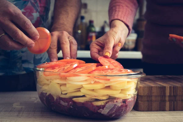 Добавление помидоров в выпечку с сырым мясом и картофелем — стоковое фото
