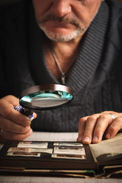 Man considers album of stamps trough the magnifying glass vertical — Stock Photo, Image