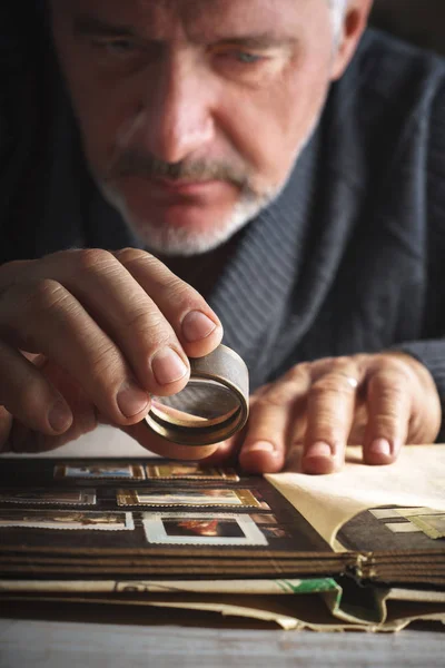 Man considers album of postage stamps trough the magnifying glass vertical — Stock Photo, Image