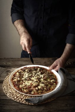 Adam bitmiş pizza üzerinde beyaz bir tabak keser.
