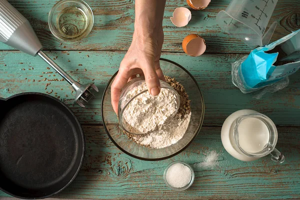 Het toevoegen van meel in glazen kom voor pannenkoeken voorbereiding bovenaanzicht — Stockfoto