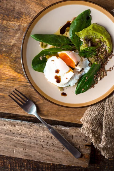 Sázená vejce s avokádovým krémem a špenátem na starý dřevěný stůl vertikální — Stock fotografie