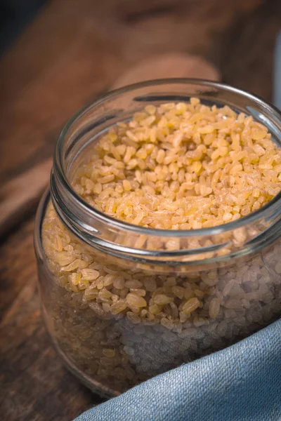 Grain bulgur in a glass jar and a spoon on the table — Stock Photo, Image