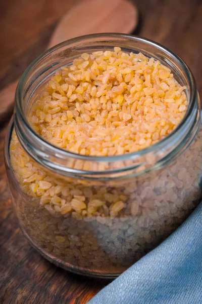 Grain bulgur in a glass jar and a napkin on the table — Stock Photo, Image