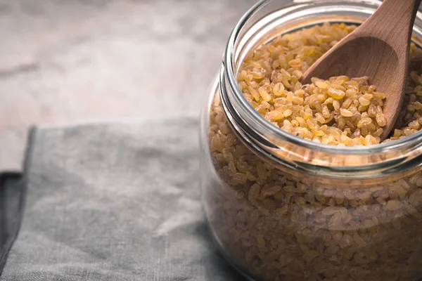 Grain bulgur in a glass jar and in a spoon close-up — Stock Photo, Image