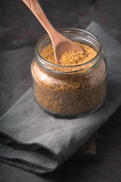 Grain bulgur in a glass jar and in a spoon on the napkin — Stock Photo, Image