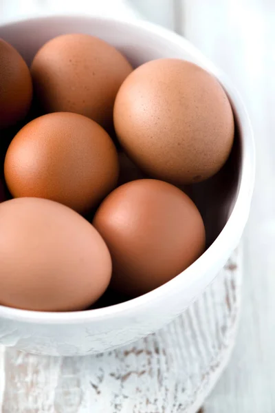 Huevos en el cuenco de cerámica en la mesa de madera blanca vertical — Foto de Stock