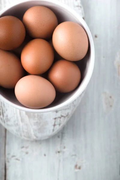 Chicken eggs  in the ceramic bowl on the white wooden table top view — Stock Photo, Image