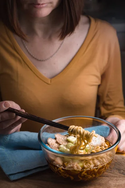 Женщина в жёлтой куртке ест суп с лапшой — стоковое фото