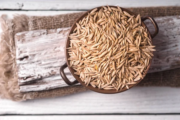 Oats in a copper bowl on a wooden stand — Stock Photo, Image