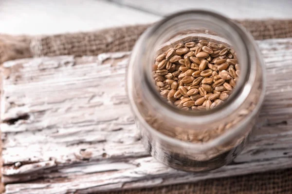 Wheat seeds in a glass jar on a white rustic board side view — Stock Photo, Image