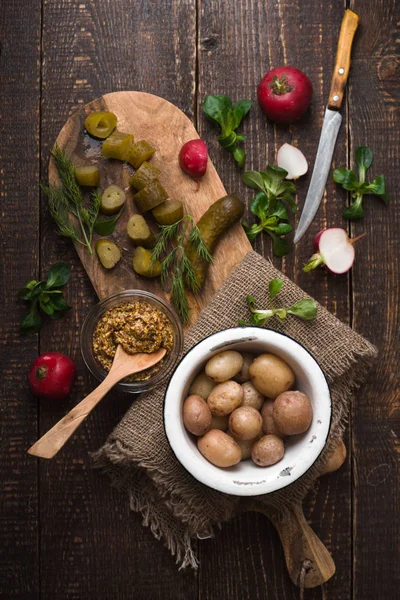 Pepino, rábanos, lechuga, mostaza, patatas en una tabla de cortar vista superior — Foto de Stock