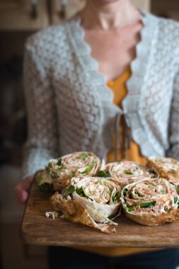 Kadının elinde ahşap tahta üzerinde ton balığı ve yeşillik ile rulo