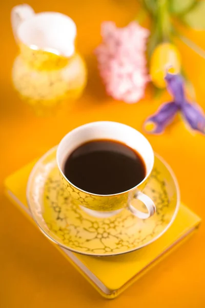 Cup with coffee, flowers, notebook on a yellow background