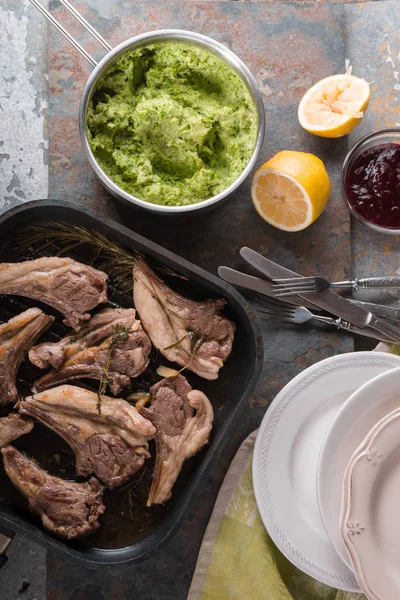 Costillas de cordero a la parrilla, puré de papas, salsa de remolacha, limón, platos, tenedores en la mesa —  Fotos de Stock