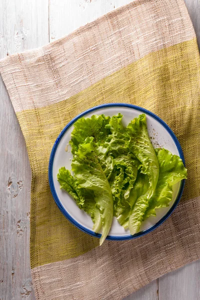 Seramik plaka üzerinde beyaz ahşap masa dikey yeşil salata — Stok fotoğraf