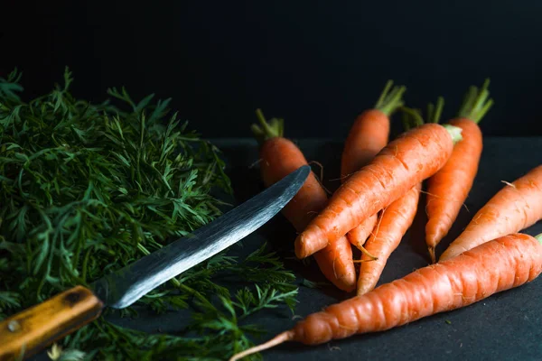 Zanahorias anaranjadas, hojas y un cuchillo sobre un fondo azul oscuro — Foto de Stock