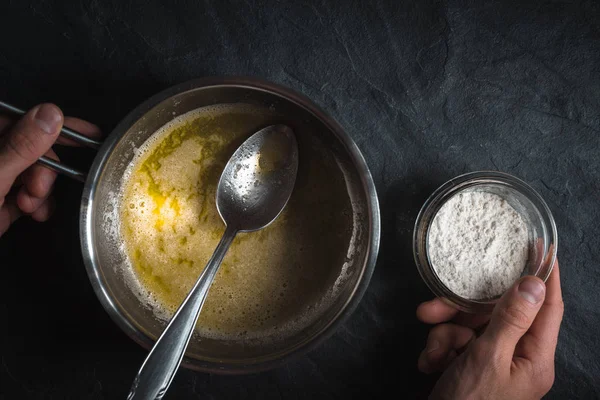 Melted butter in a ladle and a bowl of flour in a hand — Stock Photo, Image