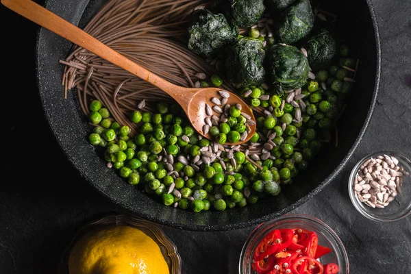 Fideos de trigo sarraceno en una sartén, guisantes congelados y espinacas, chiles y semillas en un tazón — Foto de Stock