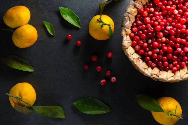 Gelbe Mandarinen mit Blättern und Preiselbeeren in einem Korb auf einem grauen Steinfreien Raum — Stockfoto