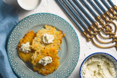 Latkeler ve lor peynir bir plaka üzerinde ve mavi peçeteye chanukia