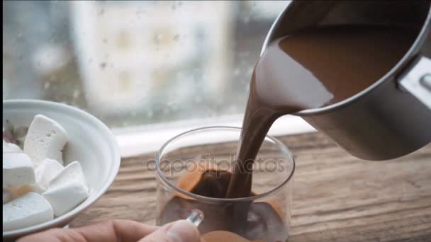Verter cacao en una taza de cacerola, marshmella en un tazón en un alféizar de ventana de madera — Vídeos de Stock