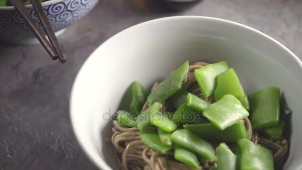 Buckwheat noodles with green beans in a ceramic bowl on a gray stone — Stock Video