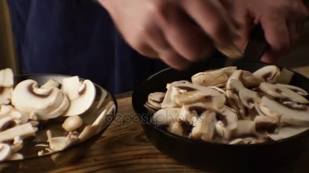 O homem desloca os cogumelos do prato para uma frigideira. Vídeo — Vídeo de Stock