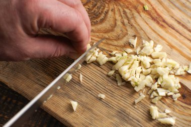 Adam bir ahşap tahta üzerinde küçük parçalara sarımsak keser