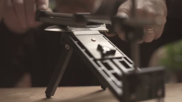 Man sharpens a kitchen knife while sitting at a table in the background of a video window — Stock Video