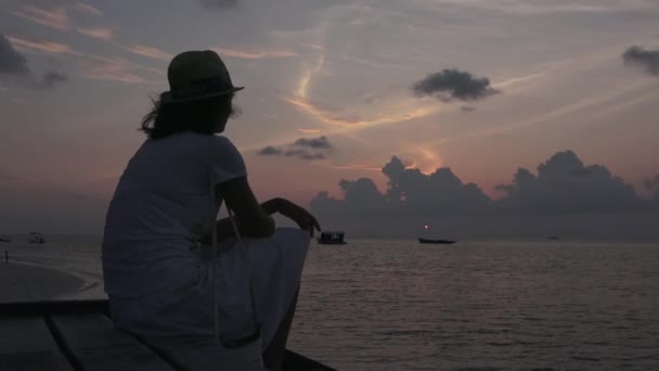 La chica se sienta en la orilla y mira el atardecer. Maldivas primer plano de vídeo — Vídeo de stock