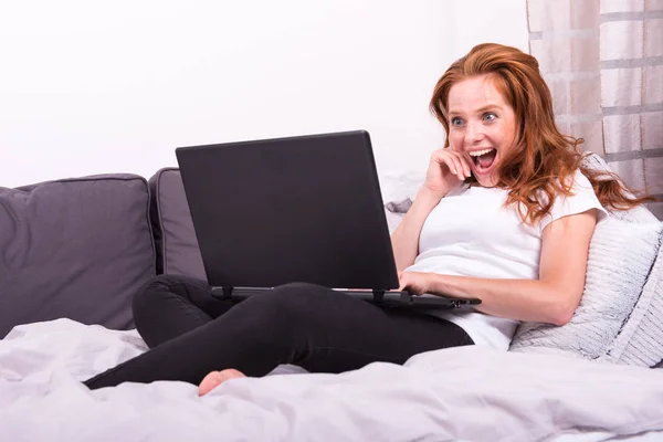 Молодая рыжеволосая женщина работает со своим ноутбуком дома на — стоковое фото