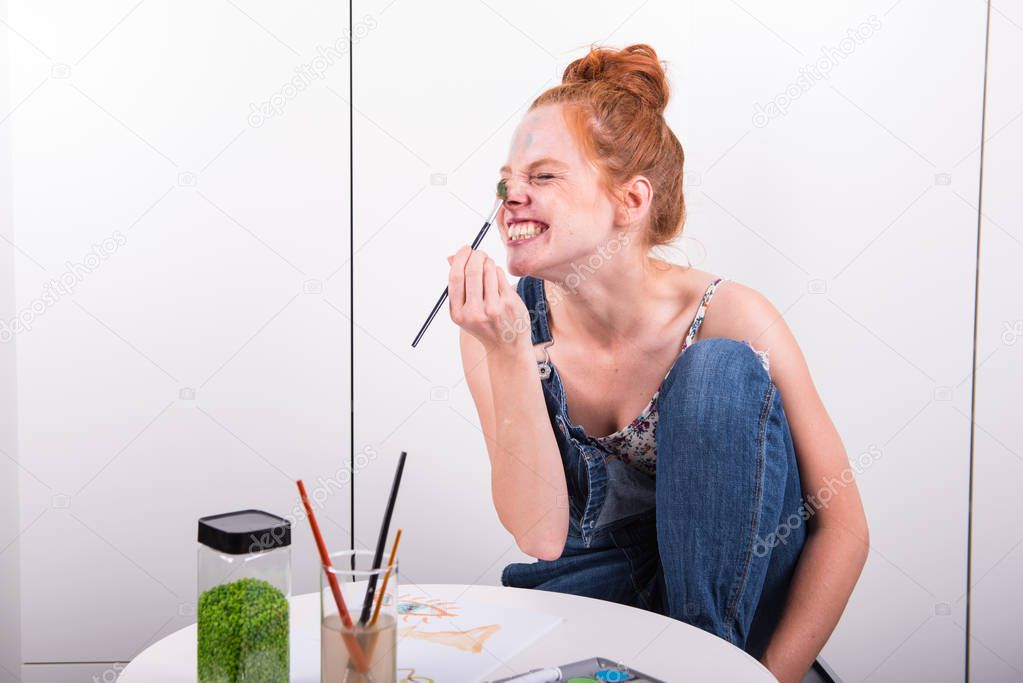 attractive redhead is making fun during painting with water colo