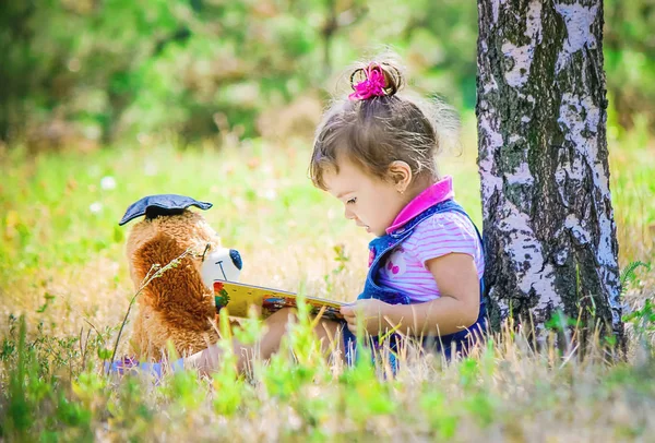 Дитина на відкритому повітрі з іграшками читає книгу. Вибірковий фокус . — стокове фото