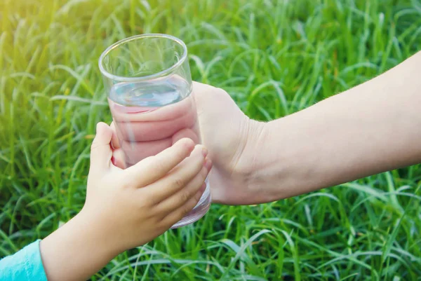 Mujer dando un vaso de agua limpia a un niño. Enfoque selectivo . — Foto de Stock