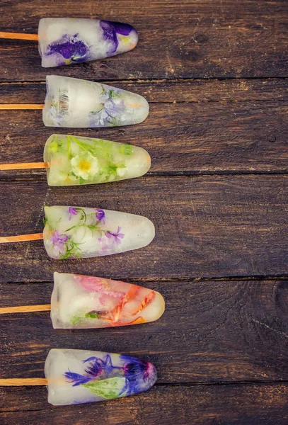 frozen flowers in ice cubes and ice cream on a stick. selective focus.