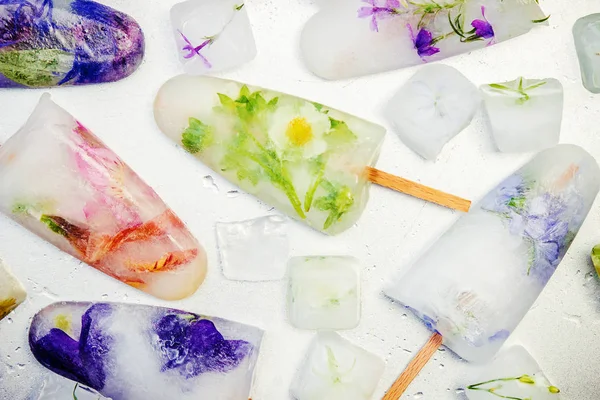 frozen flowers in ice cubes and ice cream on a stick. selective focus.