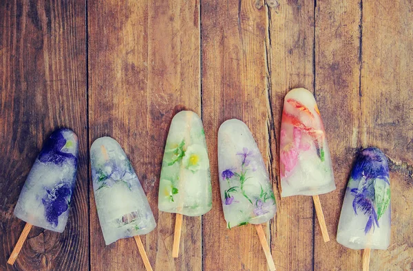 frozen flowers in ice cubes and ice cream on a stick. selective focus.