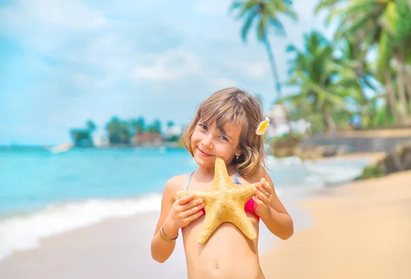 A child with a starfish in his hands on the beach. Selective focus. — Stock Photo, Image