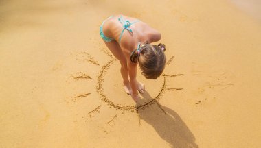 A child draws a sun on the beach. Selective focus.