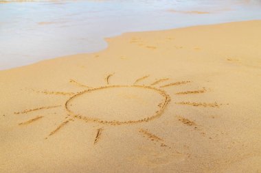 A child draws a sun on the beach. Selective focus.