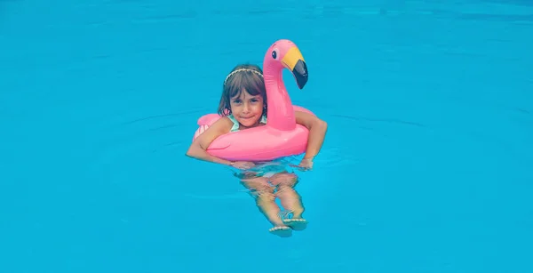 A child swims in a pool with a circle of flamingos. Selective focus. — Stock Photo, Image