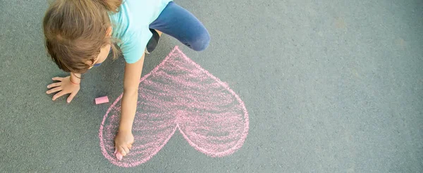 El niño pinta la tiza en el corazón de asfalto. Enfoque selectivo . — Foto de Stock