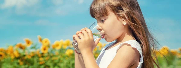 Ein Kind trinkt Wasser auf dem Hintergrund des Feldes. Selektiver Fokus. — Stockfoto