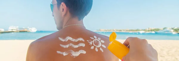 Девушка на пляже наносит солнцезащитный крем на кожу мужчины. Селективный фокус . — стоковое фото