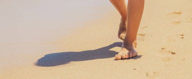 çocuk kumda ayak izleri bırakarak plaj boyunca yürür. Seçici odak. Doğa.