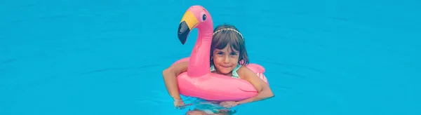 A child swims in a pool with a circle of flamingos. Selective focus.