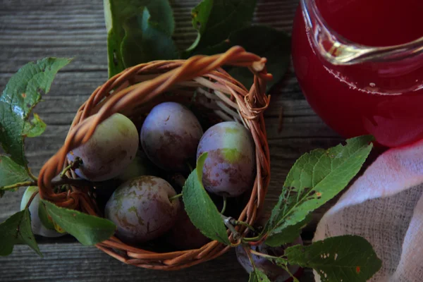 Fresh plums in a wicker basket and compote in a jar — Stock Photo, Image