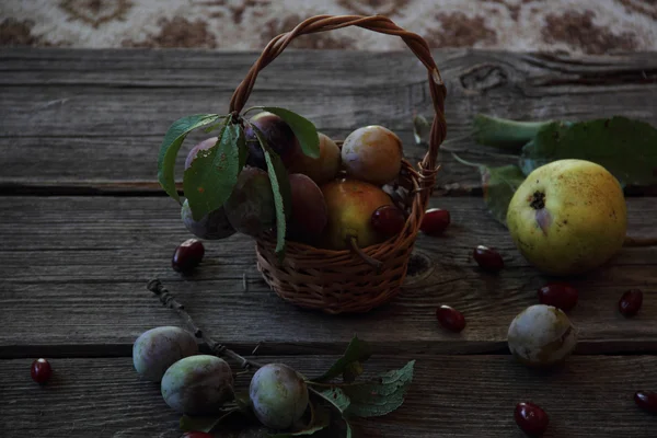 Nature morte avec des prunes fraîches dans un panier en osier et des poires — Photo